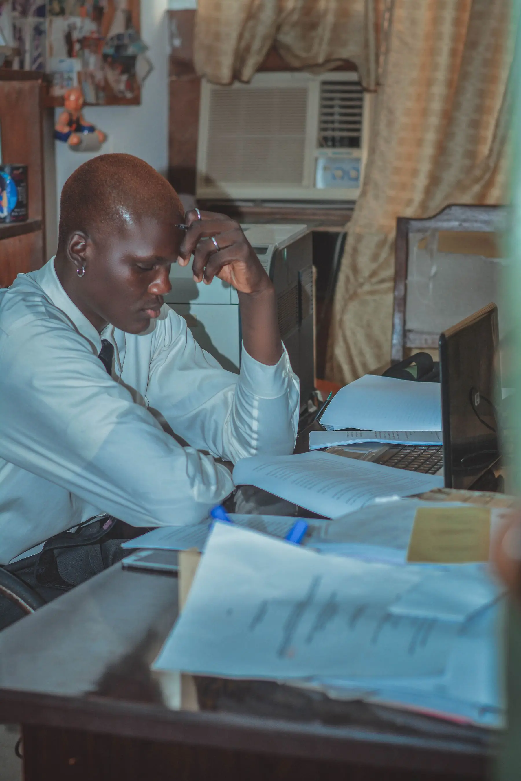 A school administrator working through stacks of paper records and ledgers beside a laptop
