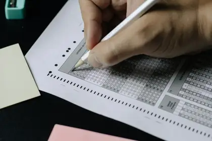 A hand shading in an answer on a multiple choice exam sheet with a pencil