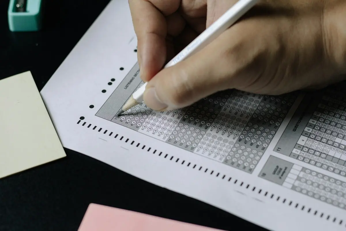 A hand shading in an answer on a multiple choice exam sheet with a pencil