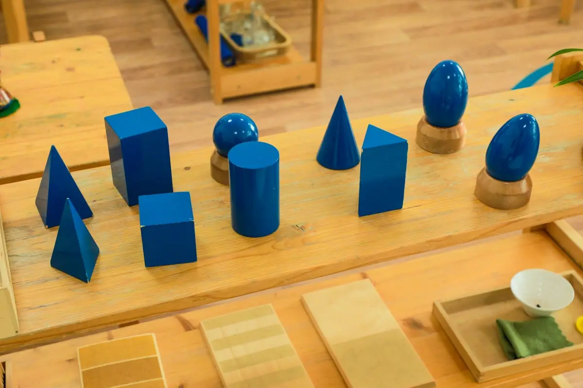 Blue wooden geometric solids on a Montessori classroom shelf