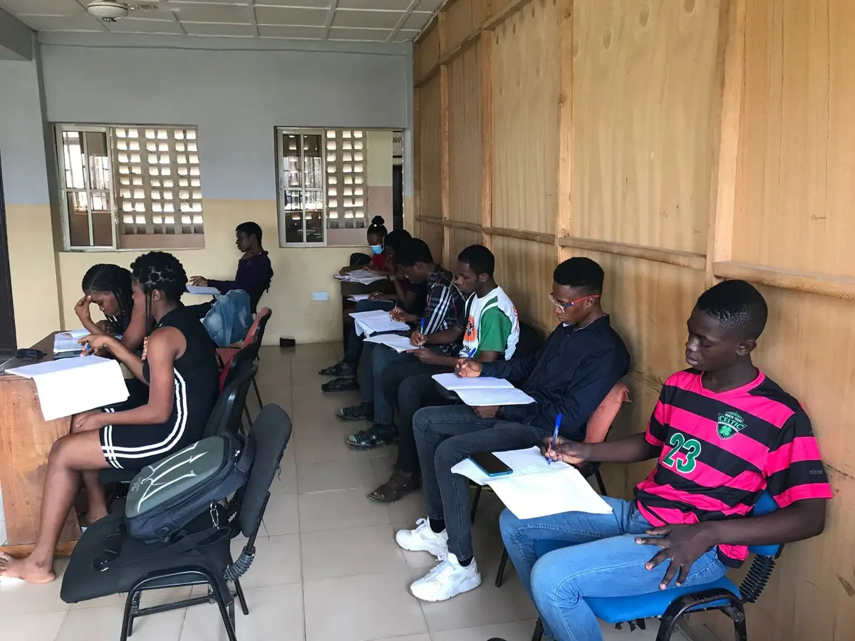 Young people sitting in a row at desks, writing in an exam room