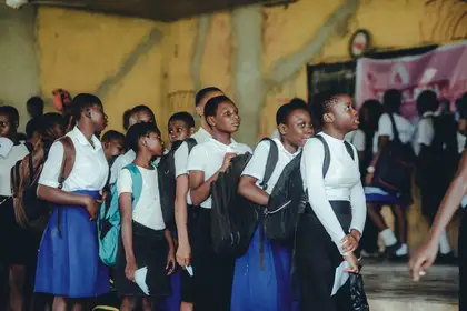 Learners in school uniform with backpacks standing together in a school hall